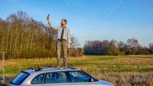 Mann steht auf einem Autodach und versucht Empfang zu finden, um zu telefonieren, weil er eine Autopanne hat