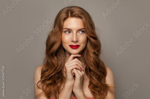 Beautiful young red-haired woman with long beauty curly hair on brown background