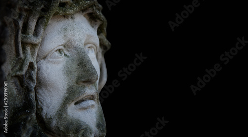 Ancient statue of the crucifixion of Jesus Christ in profile agaist black background.
