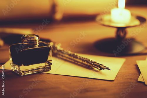 vintage quill pen and inkwell on wooden table in candlelight