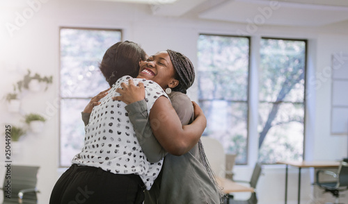 Two female black african freelancers embraced in a friendly hug in a modern co-working space