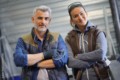 Portrait of metalworker with woman apprentice standing in workshop