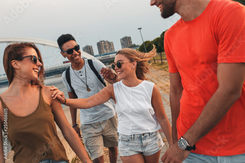 Group of young friends walking through the city by the river talking and having fun.