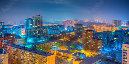 Urban panorama. Beautiful top view of the city. Colorful street lighting of the night metropolis. Many high-rise buildings. Cold winter weather. Novosibirsk, Siberia, Russia.