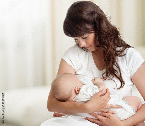 Young mother feeding breast her baby at home in white room