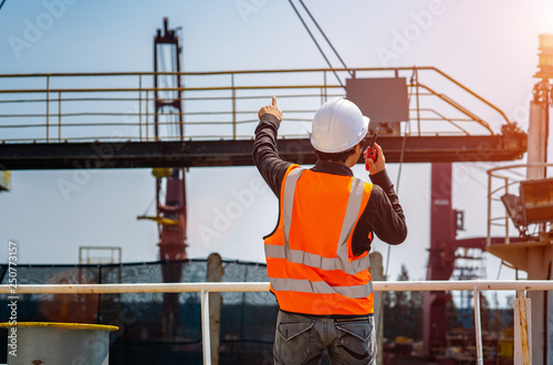stevedore or foreman, engineering, loading master talks to crane driver by walkie talkie for safety lifting the goods or shipment, lifting by gantry crane, working at risk on the high level insurance