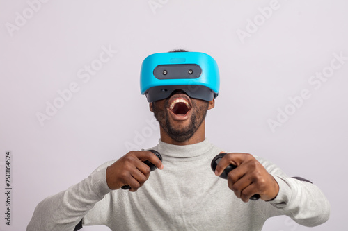 African happy overjoyed guy in VR glasses driving virtual car isolated over white background learning to drive a car. Virtual driving school or studio concept