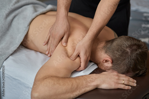 Young handsome man enjoying a back massage. Professional massage therapist is treating a male patient in apartment. Relaxation, beauty, body and face treatment concept. Home massage.