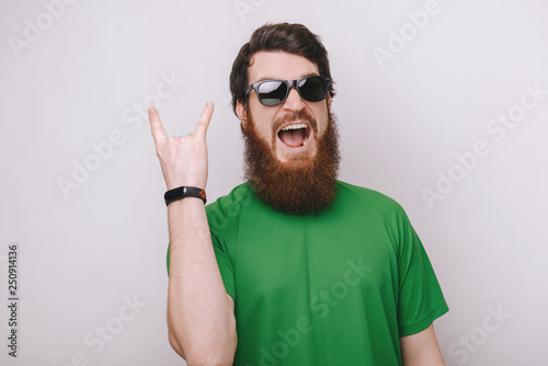 Like a rock star. Confident young man in sunglasses gesturing and keeping mouth open while standing against grey background