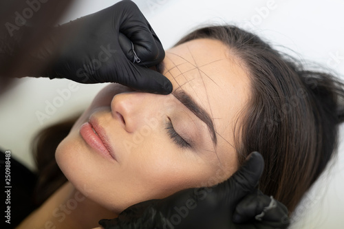 Beautician in the saloon doing the perfect architecture of eyebrows.