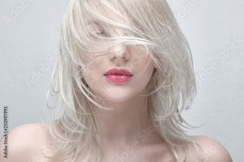 Portrait of a young beautiful blonde woman with plump red lips and bare shoulders on a white background close up. Fashionable fancy hairstyle