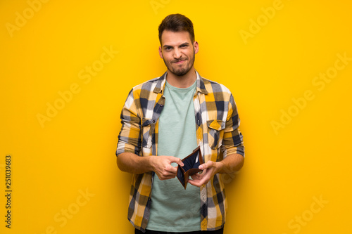 Handsome man over yellow wall holding a wallet