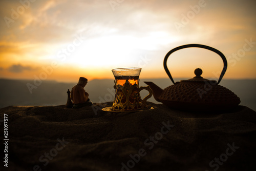 Arabic tea in traditional glass and pot on desert at sunset. Eastern tea concept. Artwork decoration on sand with tea.