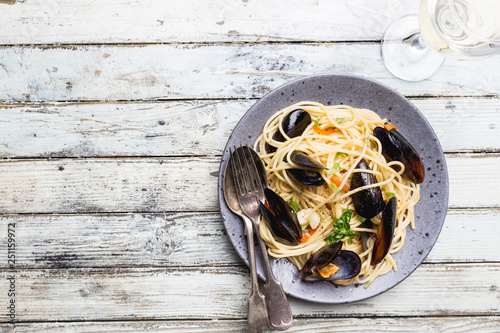 Spaghetti allo scoglio, pasta with seafood, mussels on a gray ceramic plate over wooden background, top view