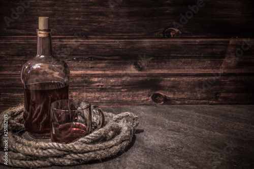 pirates bottle and glass on atone table, old rope, rum oe whiskey in transparent bottle, wooden background