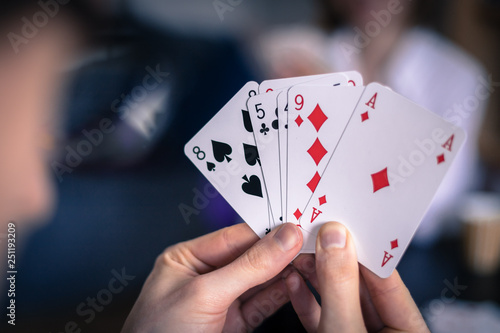 Friends are playing cards together at home. Man is holding cards in her hands, woman in the blurry background.