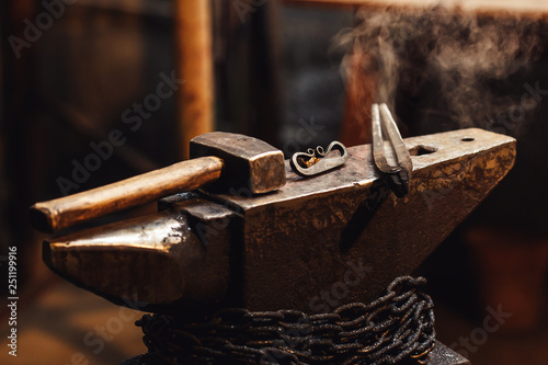 closeup of a blacksmith anvil with a hammer, tongs and firesteel.