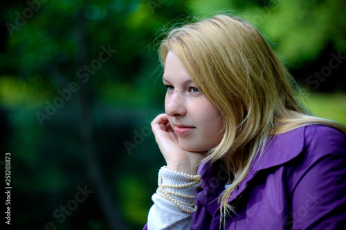 Young blonde woman in violet coat in park at summer