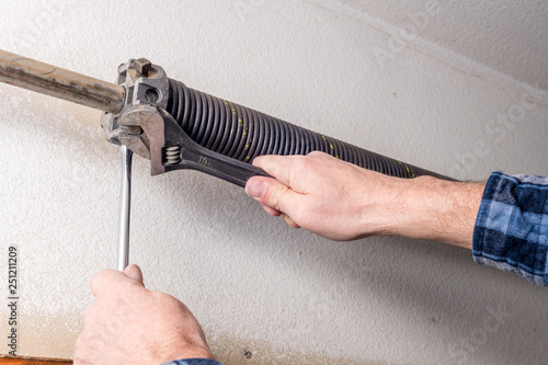 Home repairman uses tools to work on a garage door spring