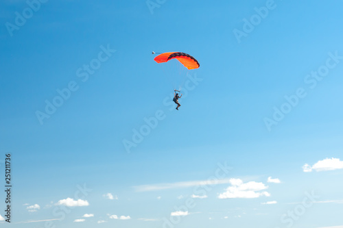 Parachutist soar on colorful parachutes across the boundless blue sky against the background of white fluffy clouds.