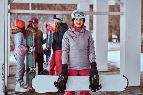 Happy redhead woman wearing winter sportswear posing with a snowboard in the winter ski resort