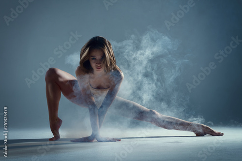 Dancing in cloud concept. Muscle brunette beauty female girl adult woman dancer athlete gymnast in smoke fog wearing dance bodysuit jumping in mid air, performance on isolated grey / black background