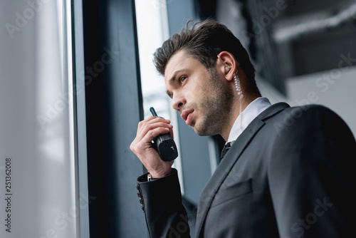 handsome bodyguard in suit using walkie-talkie