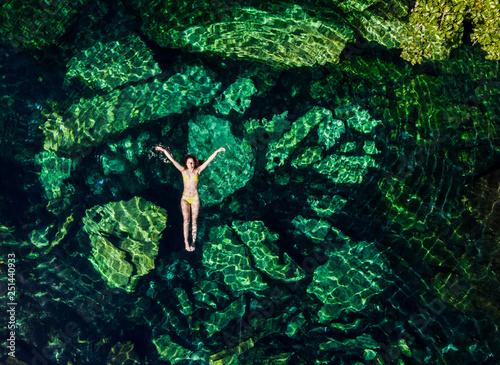 Overhead shot of a attractive young brunette woman in a bikini floating in the Cristalino cenote near Tulum, Mexico.