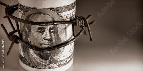 100 US Dollar bills wrapped with barbed wire as symbol of economic warfare, sanctions and embargo busting