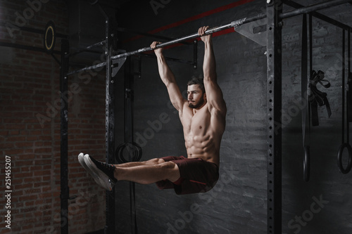 Crossfit athlete doing abs exercise on horizontal bar at the gym. Handsome man doing functional training workout. Practicing calisthenics.