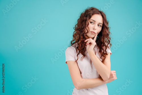 Attractive brunette girl with curly hair isolated over blue turquoise background thinking and making decision looking at copyspace