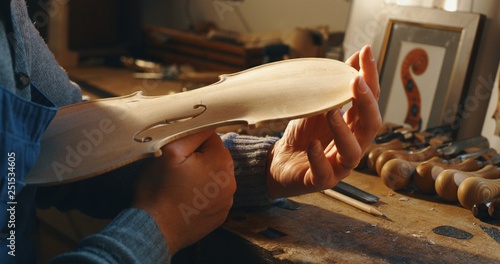 Close up of professional master artisan luthier painstaking detailed work on wood violin in a workshop.