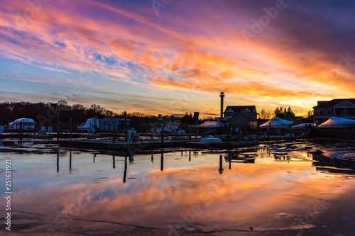 Vibrant pink and orange pastel colored clouds during a sunset. Coastal village and fishing pier reflected in the water. 