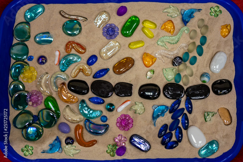 .A tray of sand, and multi-colored pebbles, figurines, seashells and ornaments laid out on it. Creative, exclusive, child's work. Suitable for illustrations in the design of children's themes.