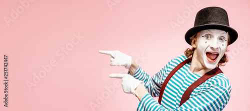 Emotional pantomime with white facial makeup showing empty space of the pink background, advertising something