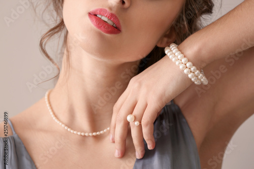 Young woman with beautiful pearl jewelry on light background, closeup