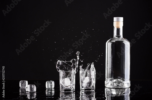 bottle of vodka with glasses and splashes on a black background