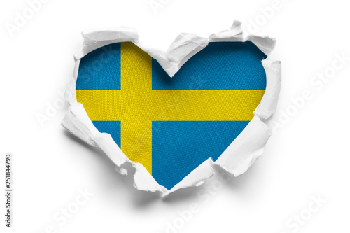 Heart shaped hole torn through paper, showing satin texture of flag of Sweden. Isolated on white background