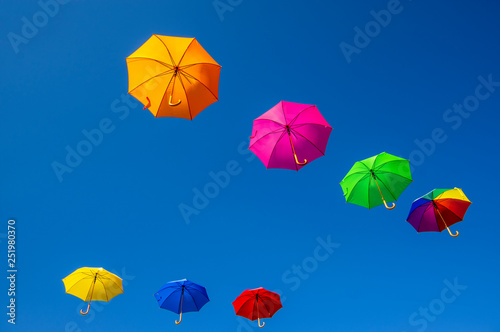 Group of flying umbrellas isolated on blue background, ready for the rain, wallpaper background, bright various colors