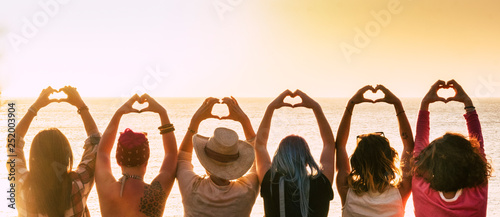 Group of diversity alternative young woman enjoying the sunset at the sea doing hearth symbol with hands - people enjoying friendly lifestyle - vacation in friendship concept for females