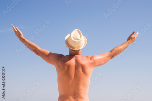 Man Raising His Hands or Open arms standing back looking to sea blue sky horizon. Strong muscular Men, perfect body, arms, back. Freedom Concept