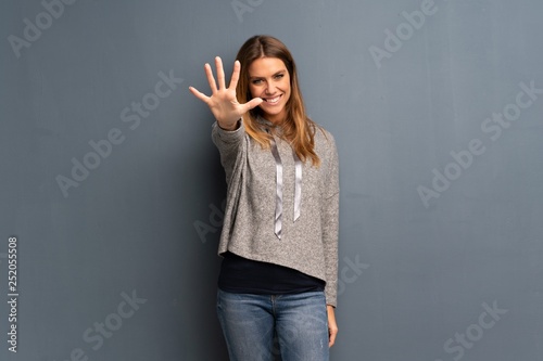 Blonde woman over grey background counting five with fingers