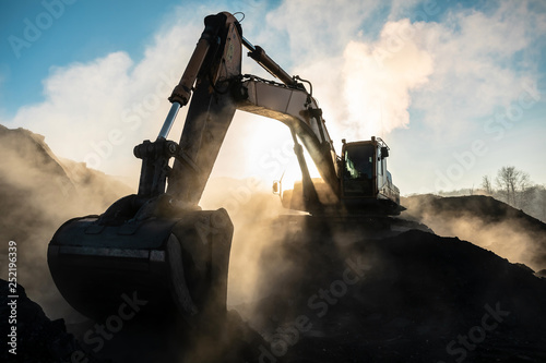 Yellow big excavator in the coal mine, loads the breed, with the bright sun and nice blue sky in the background. Mining truck mining machinery. Technique in coal mine