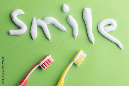 Toothpaste text with red and yellow toothbrushes on green. White toothpaste letters on green.
