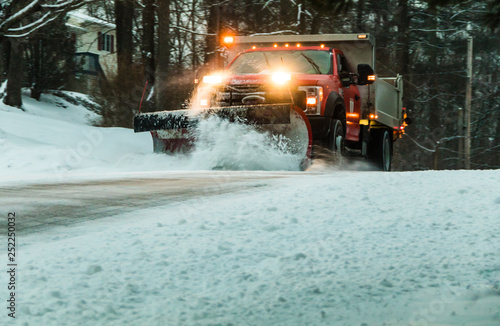 Snow plow at dusk during maintaining road in a winter storm in a residential neighborhood