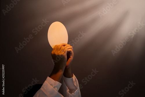 Hands of priest raise sacramental bread under light