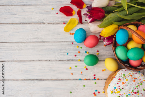 Colorful easter eggs,cake,spring tulips on wooden texture background.On a white wood table,colored eggs,flowers,bread.Happy religious day,traditional for people. Top view.Copy space.