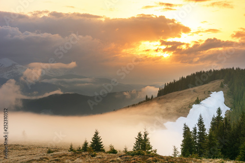 Magic spring fogs in Ukrainian Carpathians overlooking the snow-capped mountain peaks from the picturesque mountain valley with tourists in tents.