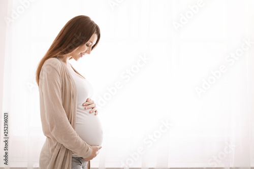 Beautiful pregnant woman hugging her tummy at home