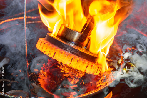 closeup calcining hot metal steel gear parts in a factory induction furnace with smoke